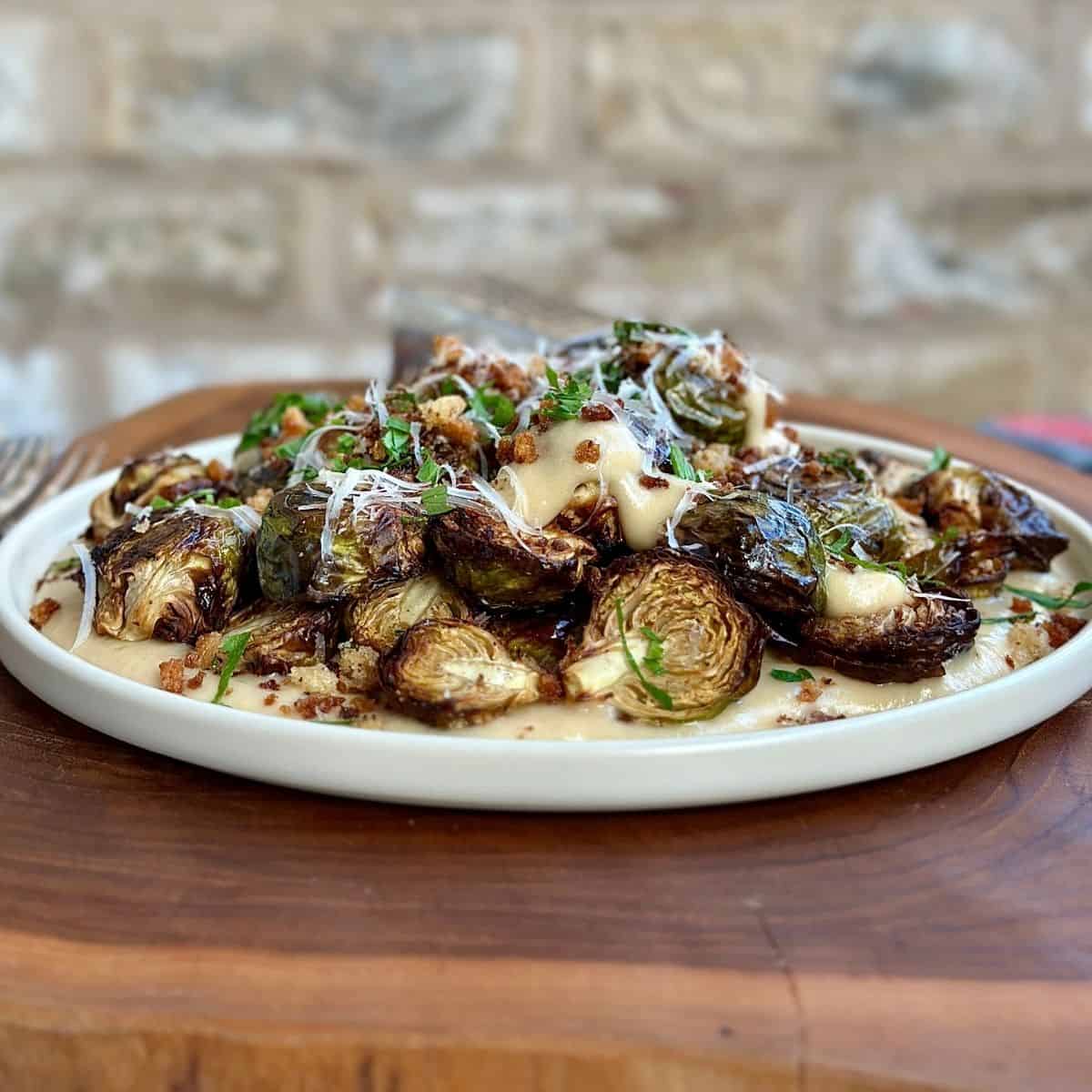 Crispy roasted Brussels sprouts with a vegan cheese sauce garnished with grated vegan Parmesan cheese on a white ceramic plate,