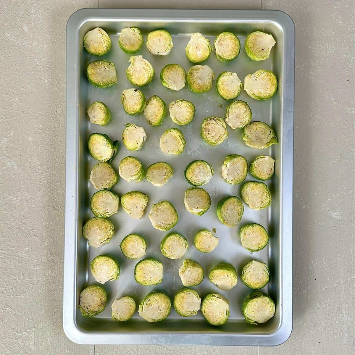 A baking tray containing Brussels sprouts cut in half with cut side facing up, ready to roast in the oven.