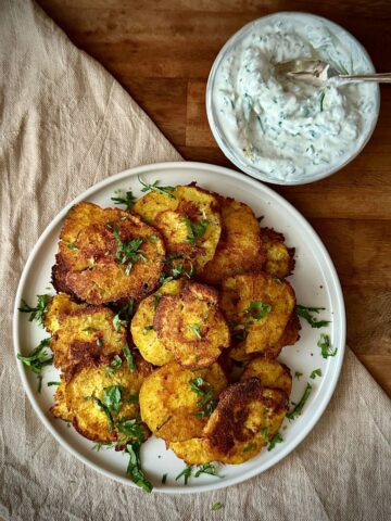 A white ceramic plate with a pile of smashed roast parsnips with a smaller dish containing a yoghurt tahini dip next to it.