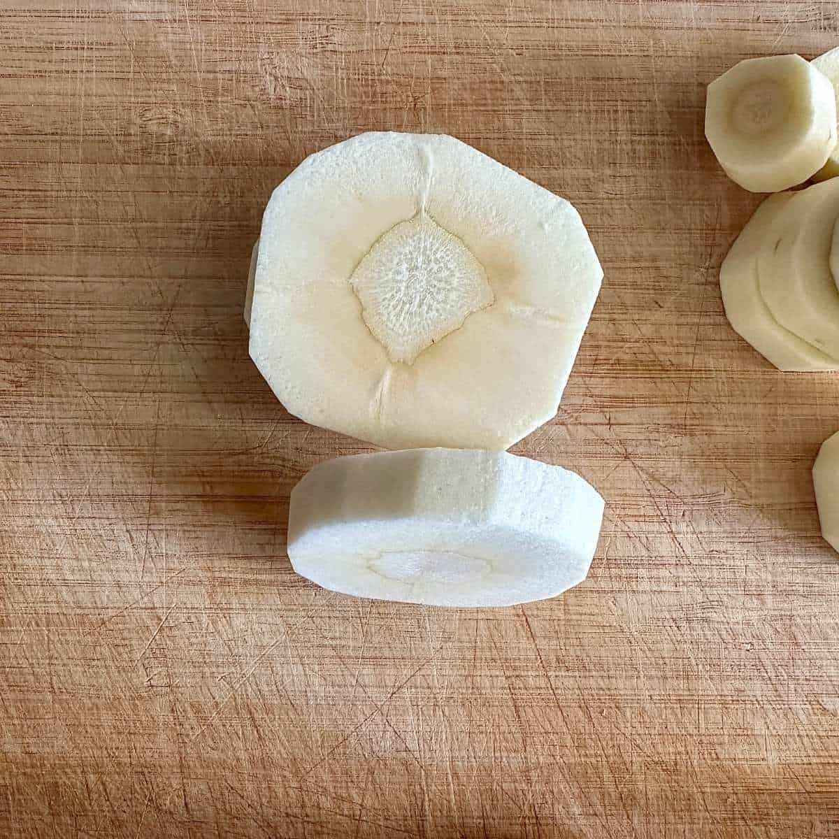Close-up of two slices of peeled parsnip, both 1-inch thick. One slice lays flat and the other sits on its edge to show the thickness.