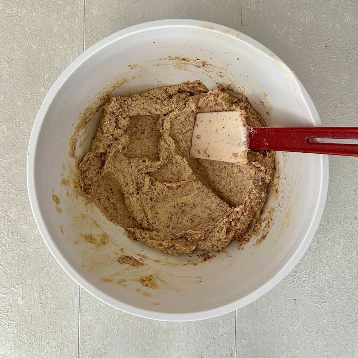 A white bowl containing creamed vegan butter and soft brown sugar with flax-egg and ground almonds mixed in. A spatula sits in the mixture.