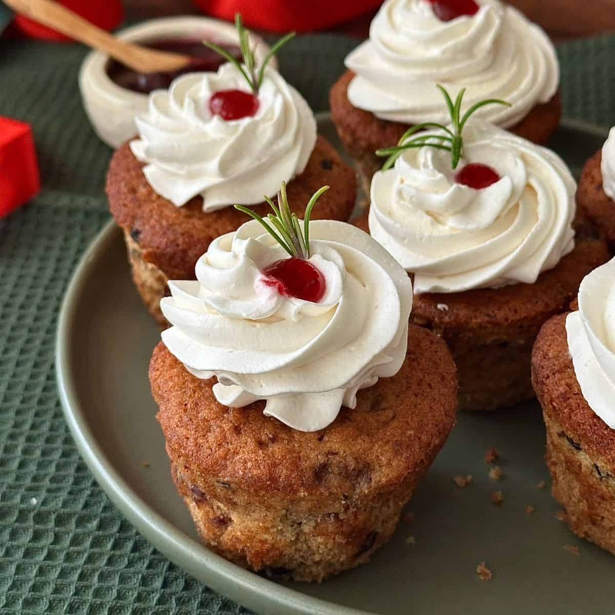 Six vegan Christmas cupcakes with brandy frosting sat on a green ceramic plate.