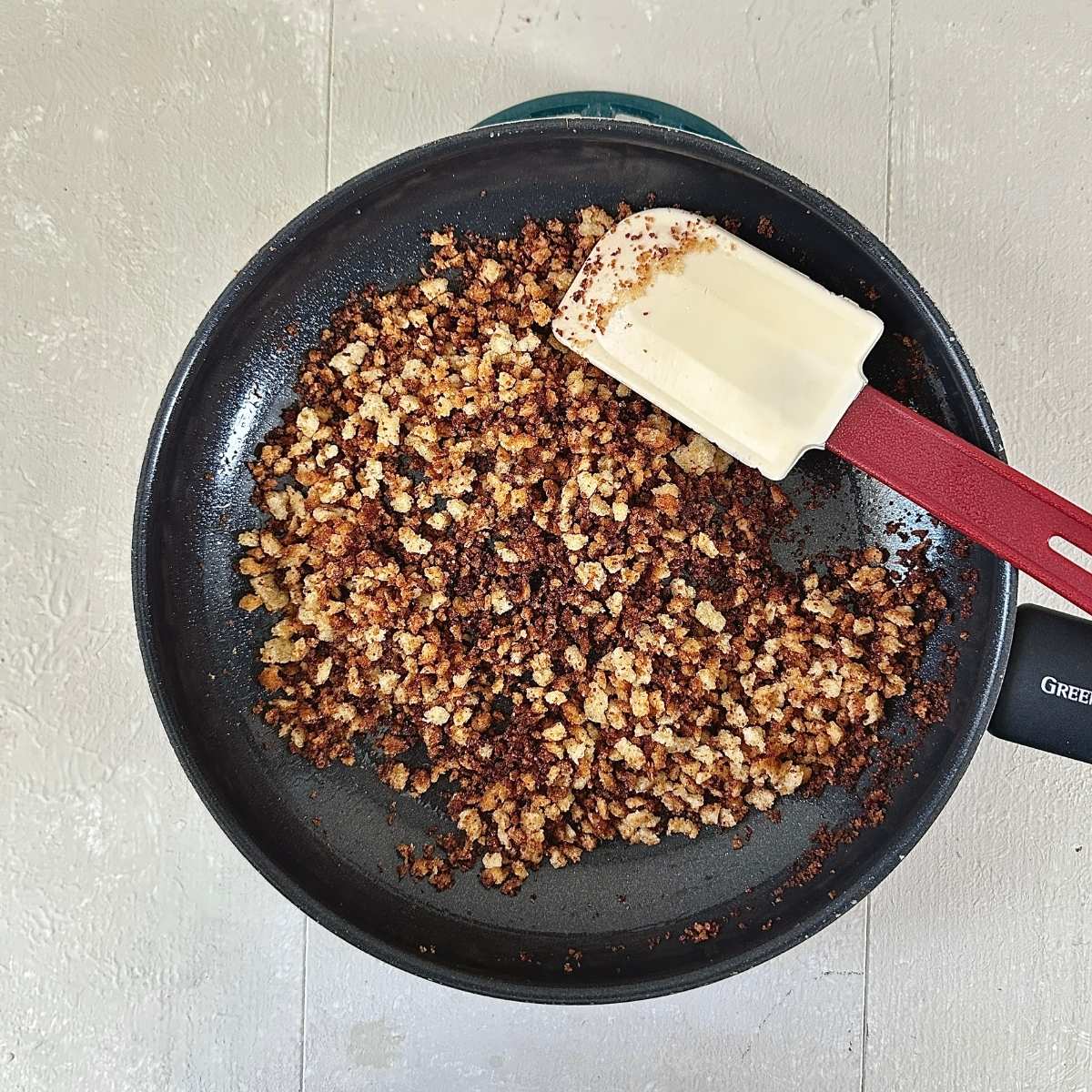 A frying pan containing fried sourdough breadcrumbs. A spatular sits in the frying pan.