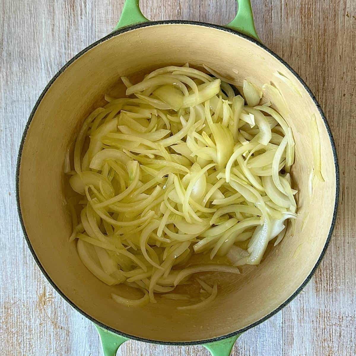 A large green pot containing thinly sliced onion for caramelised onion and leek soup recipe.