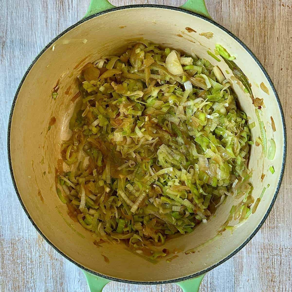 A large green pot containing cooked caramelised onion and thinly sliced leek for onion and leek soup.
