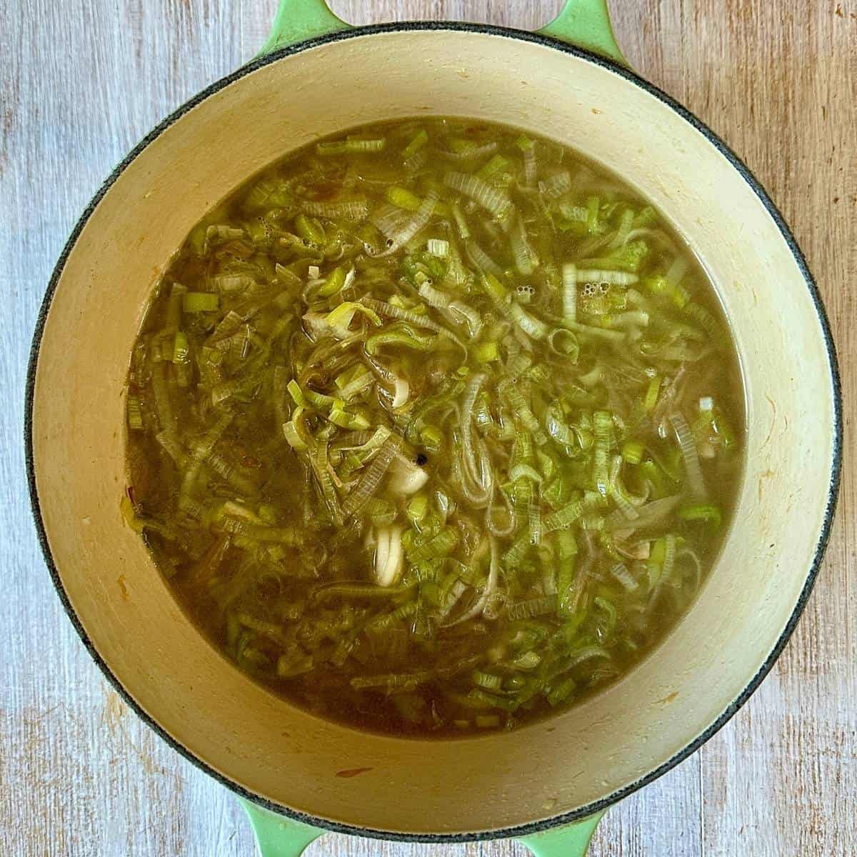 A large green pot containing caramelised onion and finely sliced leek in vegetable stock, for onion and leek soup.