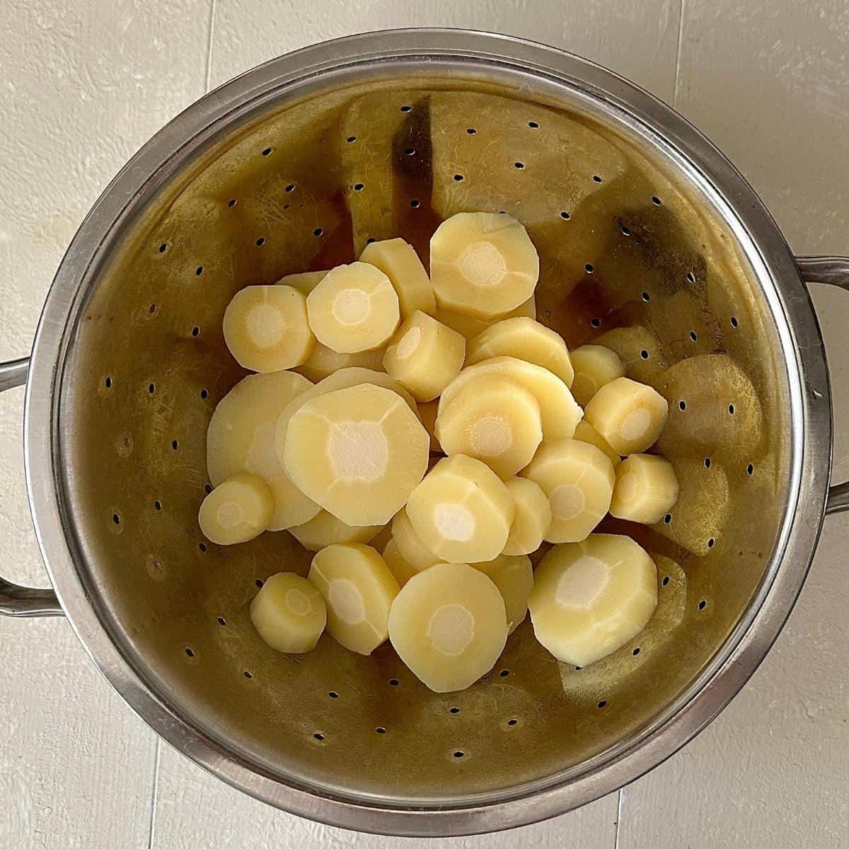 A colander containing par-boiled parsnip slices for smashed roast parsnip recipe.
