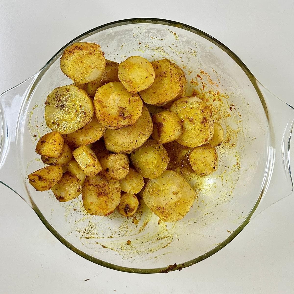 A glass bowl containing par-boiled parsnip slices coated in turmeric and cumin powder and olive oil, ready for roasting.