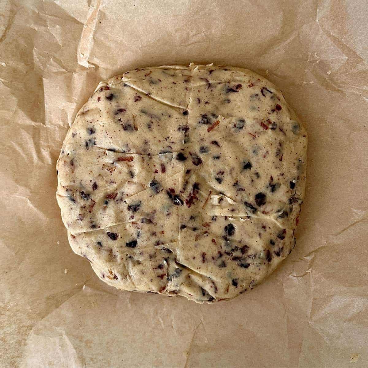 Vegan Christmas biscuit dough slightly flattened to a rough disk, sitting on top of parchment paper.