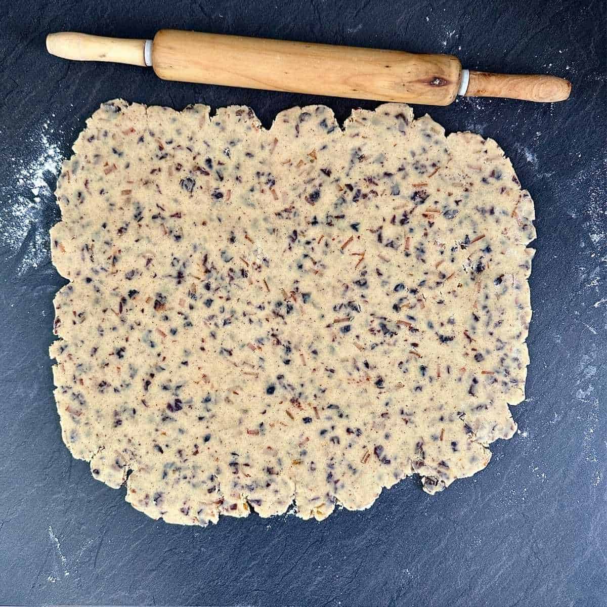 Vegan Christmas biscuit dough rolled out to 3mm thickness on a grey counter top dusted with flour.