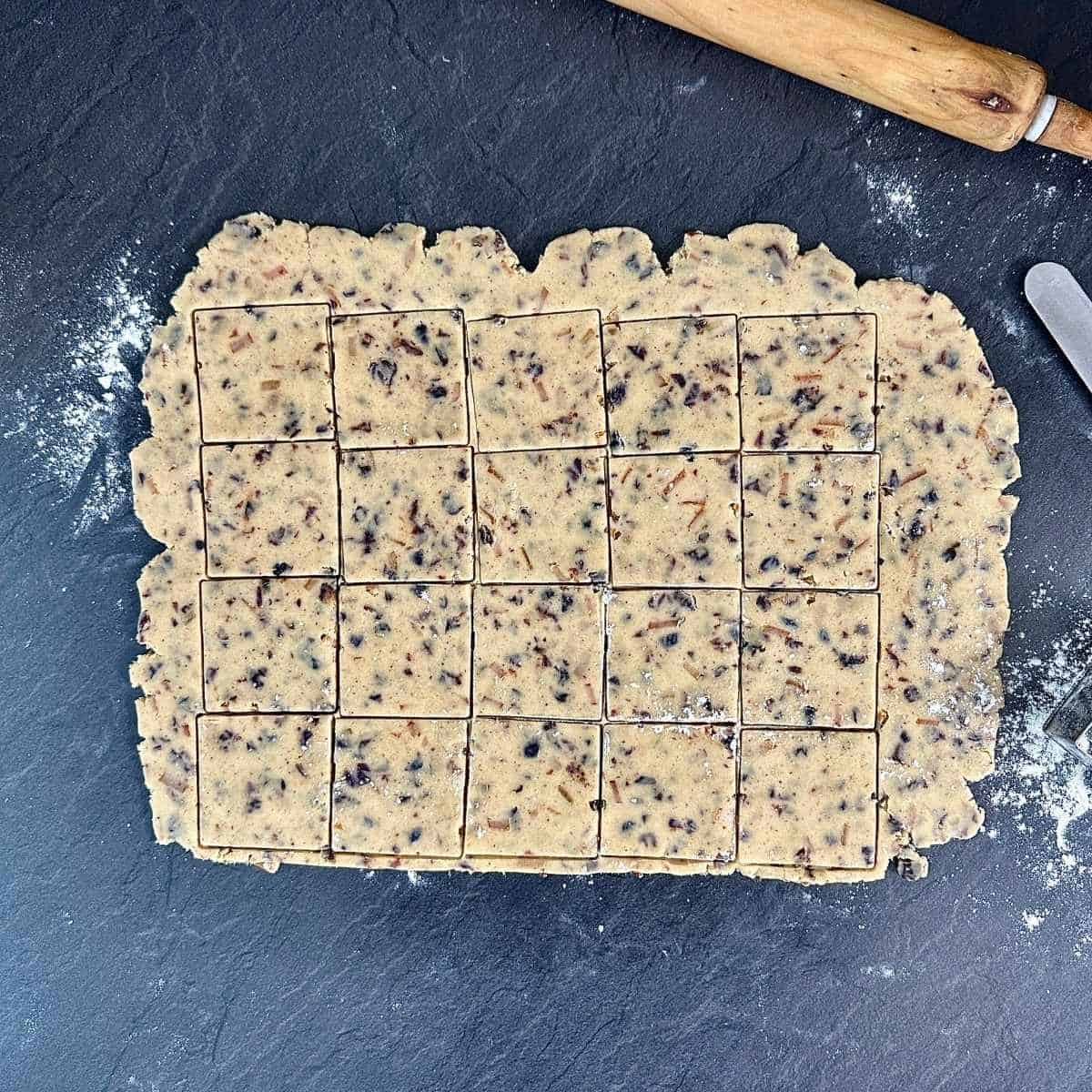 Vegan Christmas biscuit dough stamped out with a square shaped cookie-cutter, ready to transfer to a baking tray for baking.