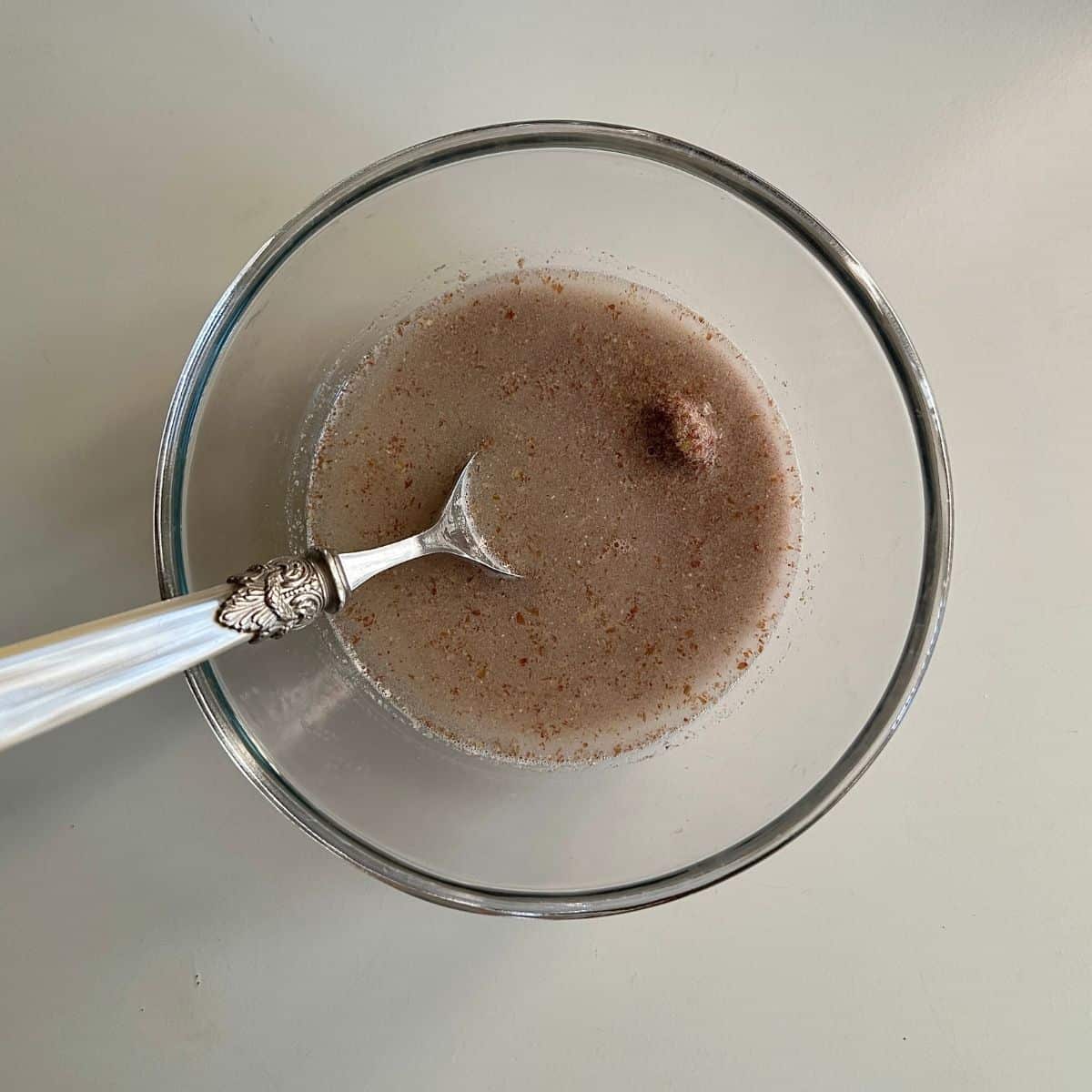 A glass bowl containing water and flaxseed powder to make flax-egg for vegan Christmas cupcakes. A spoon sits in the bowl.