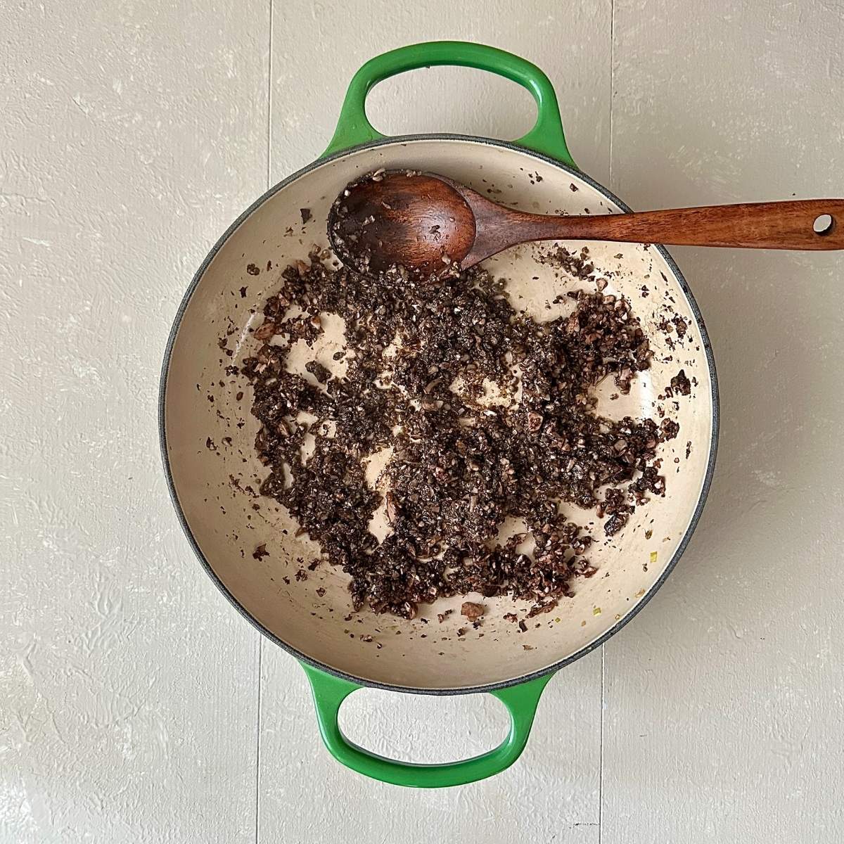 A large green saucepan containing finely chopped fried chestnut mushrooms.