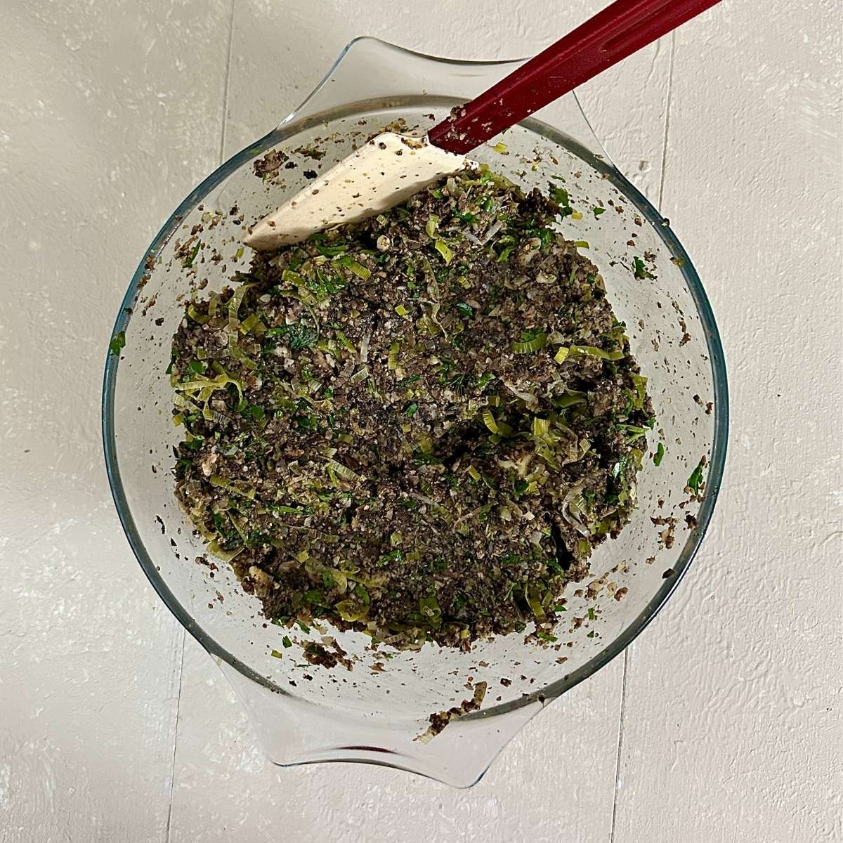 A glass bowl containing a leek, mushroom and vegan cheddar mix bound with breadcrumbs and flaxseed, ready to make vegan Christmas bake.