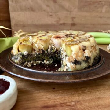 A vegan leek and mushroom Christmas bake on a serving dish with a slice removed, showing the inside of the savoury cake.