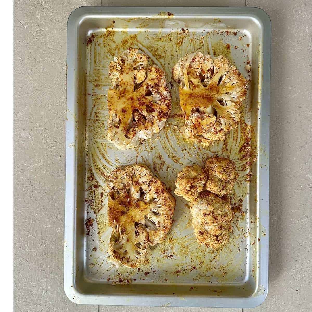 A baking tray with 4 cauliflower steaks coated in oil and cumin powder, ready to bake.