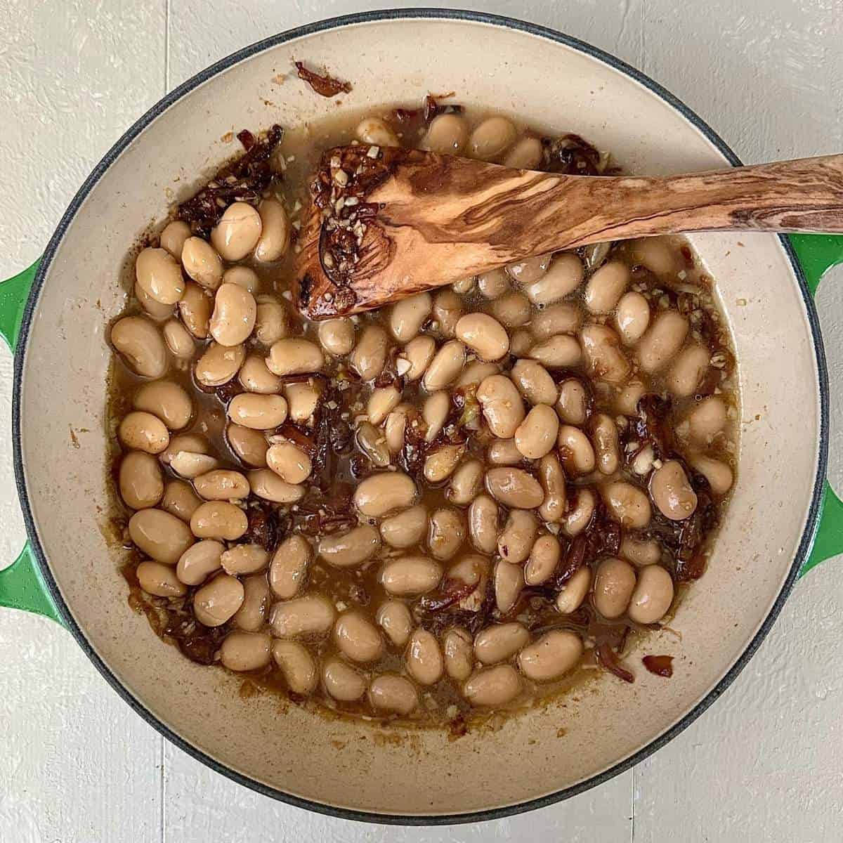 A large pot containing cooked onion and butterbeans for a korma-style sauce for roasted cauliflower steaks.