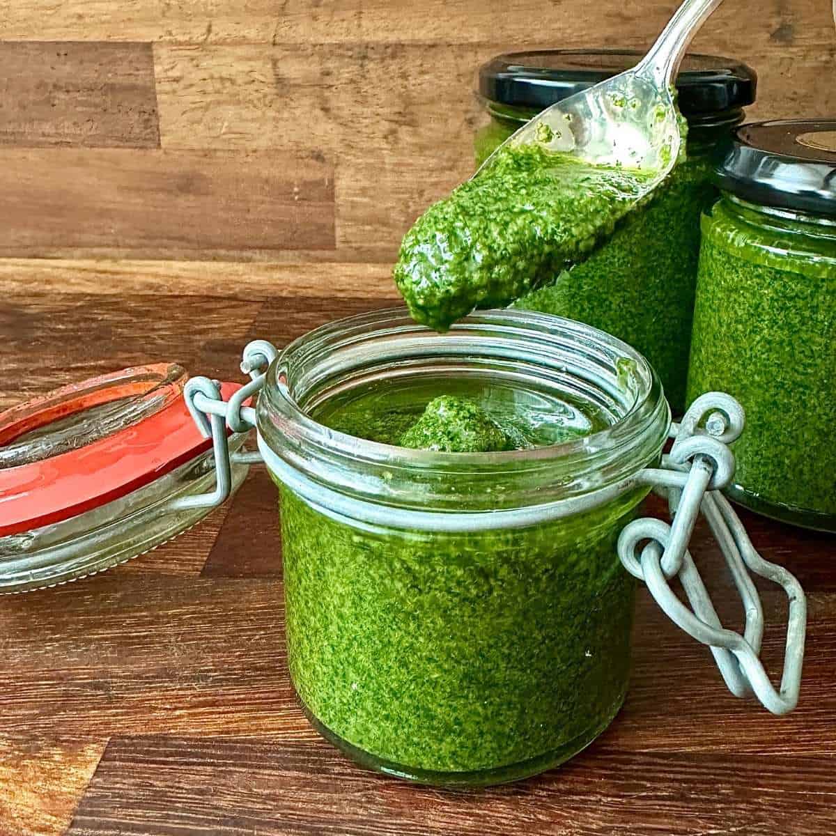 A small glass jar with a hinged lid contains a vibrant green herb sauce. A teaspoon is held above the jar with herb sauce on it.