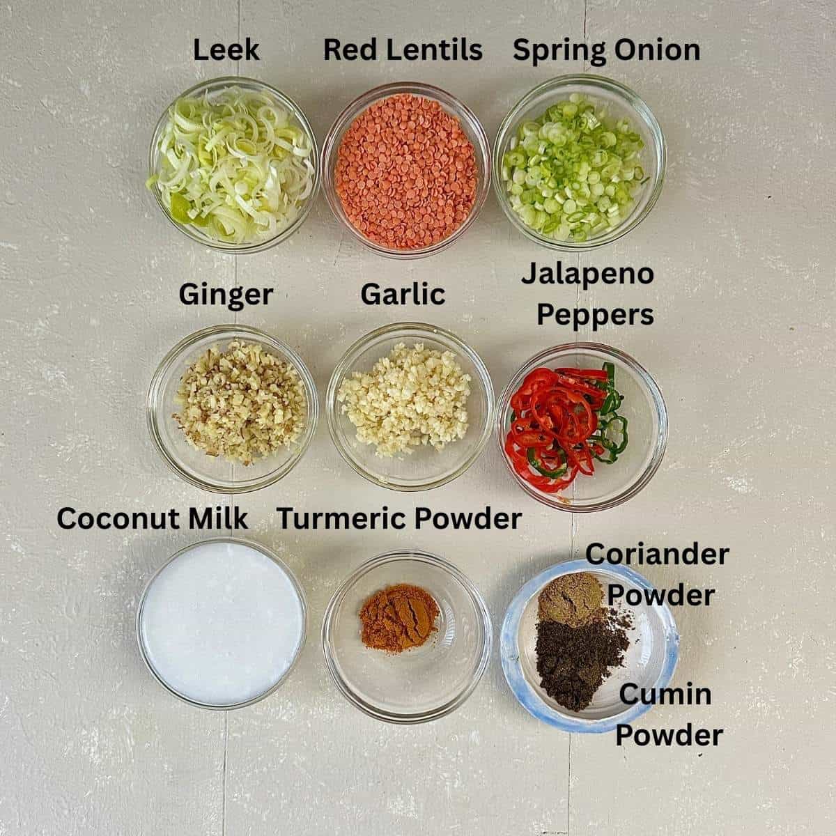 Prepared ingredients for leek and lentil soup in small glass bowls. Ingredients are annotated.