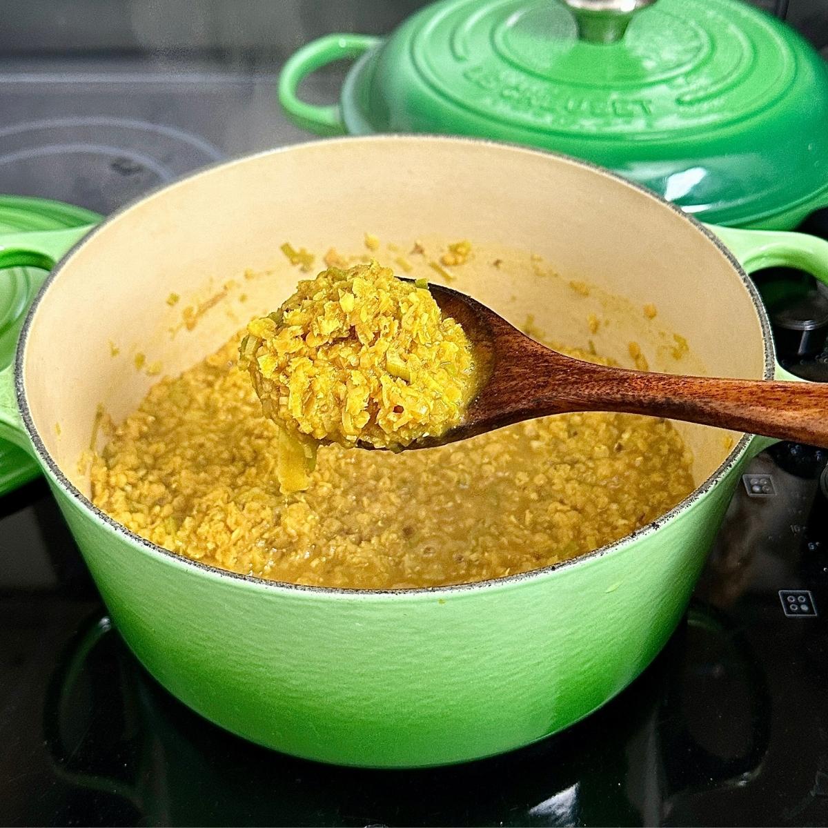 A large green post containing cooked leek and lentil soup. A spoon is help over the pot containing some of the soup to show consistency and texture.