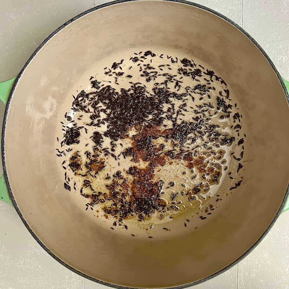 Spices frying in olive oil in a large green pot - cumin seeds and asafoetida, for pinwheel samosa