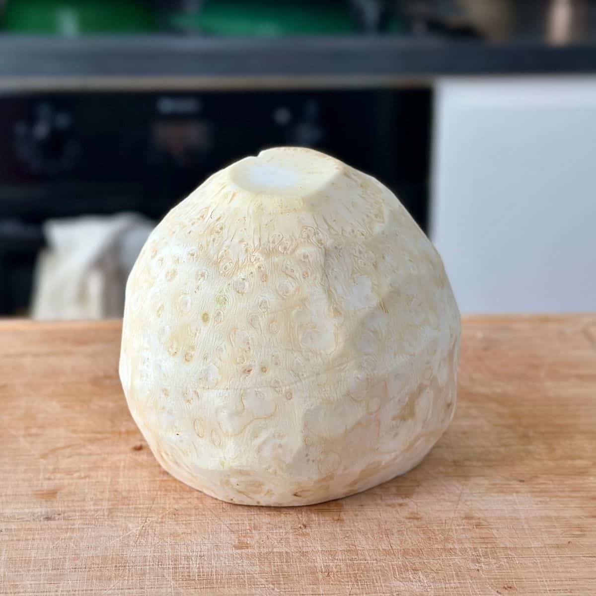 A whole, peeled celeriac sitting on a wooden chopping board.