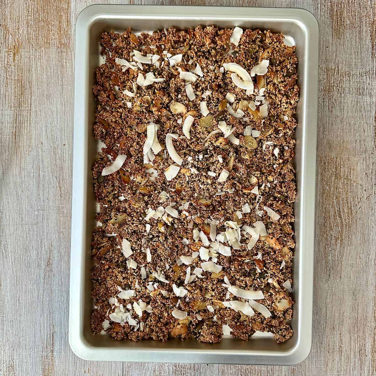 A baking tray containing sugar free granola mix, with coconut flakes added, ready to cook in the oven.