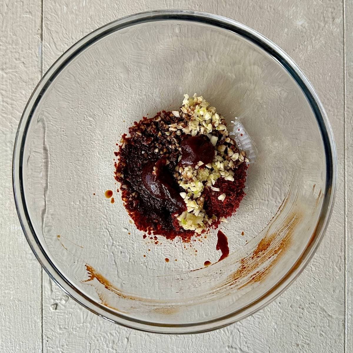 A glass bowl containing gochugaru, soy sauce, garlic and gochujang for veggie kimchi jjigae.