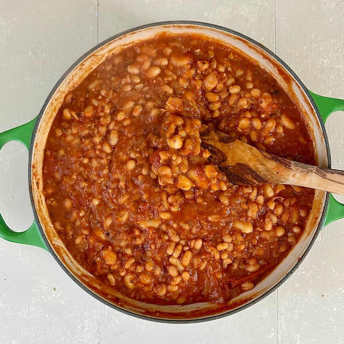 A large shallow green pot containing cheesy pizza bean ingredients after baked beans, cannelloni and haircut beans added to the chopped tomato sauce base.
