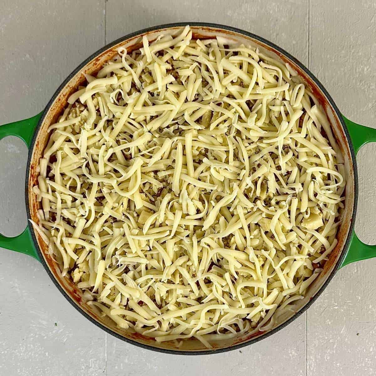 A large shallow green pan containing pizza beans with grated vegan cheddar and mozzarella cheese, ready to be baked the oven.