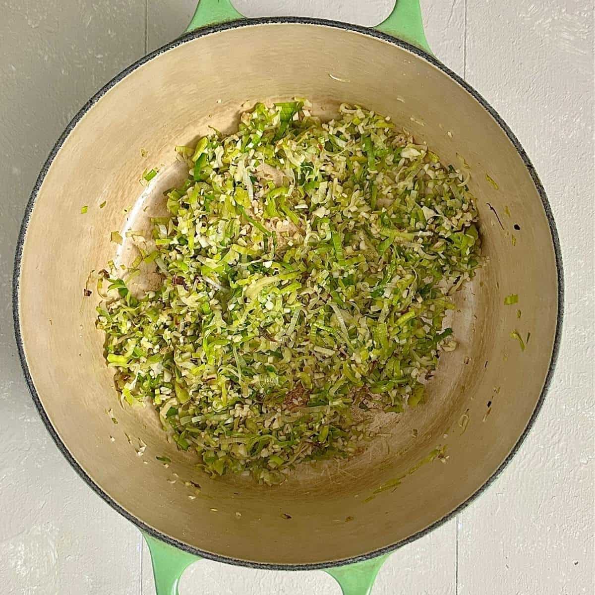 A large green pot containing finely sliced leek, ginger and garlic for leek and lentil soup.