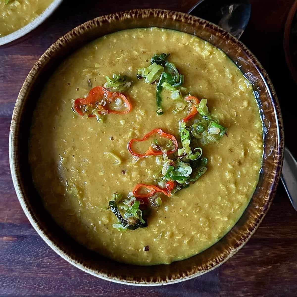 A brown rustic bowl containing leek and lentil soup garnished with fried slices of jalapeรฑo peppers and spring onion.