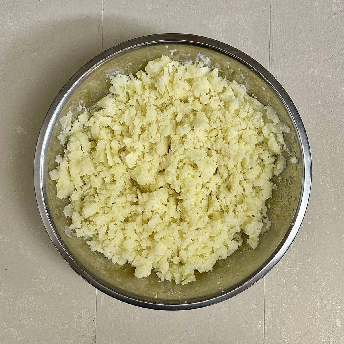 A round metal bowl containing mashed potato for pinwheel samosa.