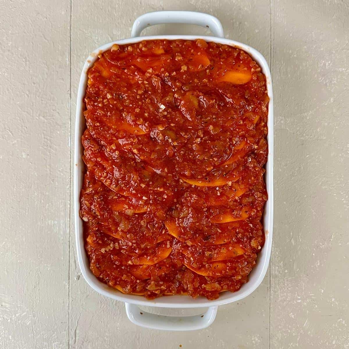 A white casserole dish containing layers of butterbean passata sauce and crown prince pumpkin.