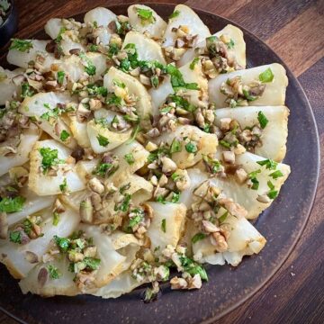 Close up of a plate of carpaccio-style roasted celeriac with an orange chestnut and walnut dressing garnished with parsley.