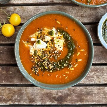 A bowl of tomato, leek and red pepper soup, garnished with seeds and pesto, with chunks of torn mozzarella in the soup.