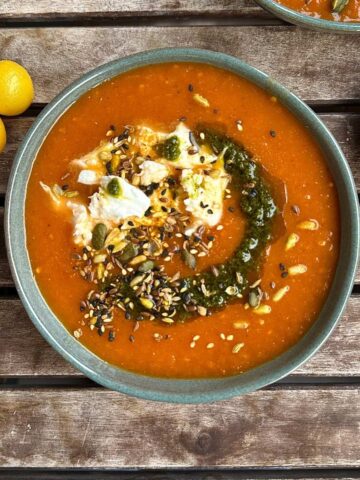 A bowl of tomato, leek and red pepper soup, garnished with seeds and pesto, with chunks of torn mozzarella in the soup.