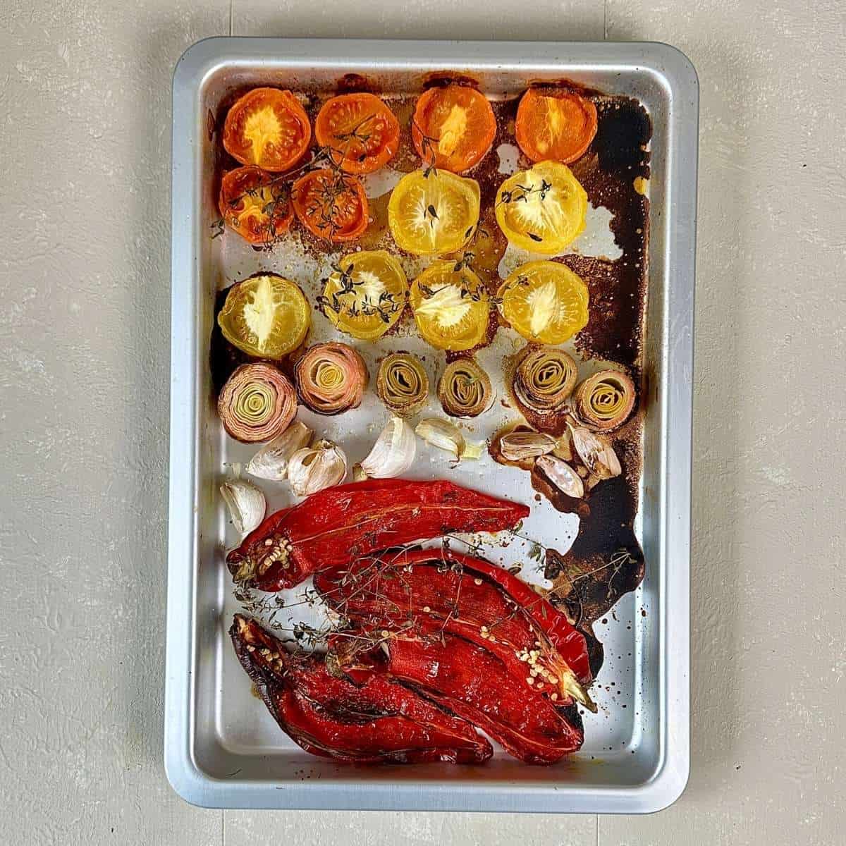 A sheet pan (baking tray) containing red peppers, leeks, and tomatoes after roasting for roasted tomato, leeks and red pepper soup.