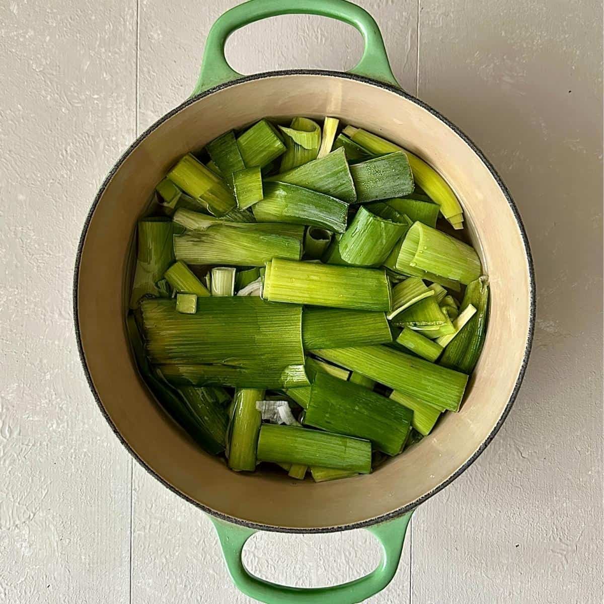 A large green pot containing the green parts of leeks in water, ready to make vegetable stock for tomato, leek and red pepper soup.