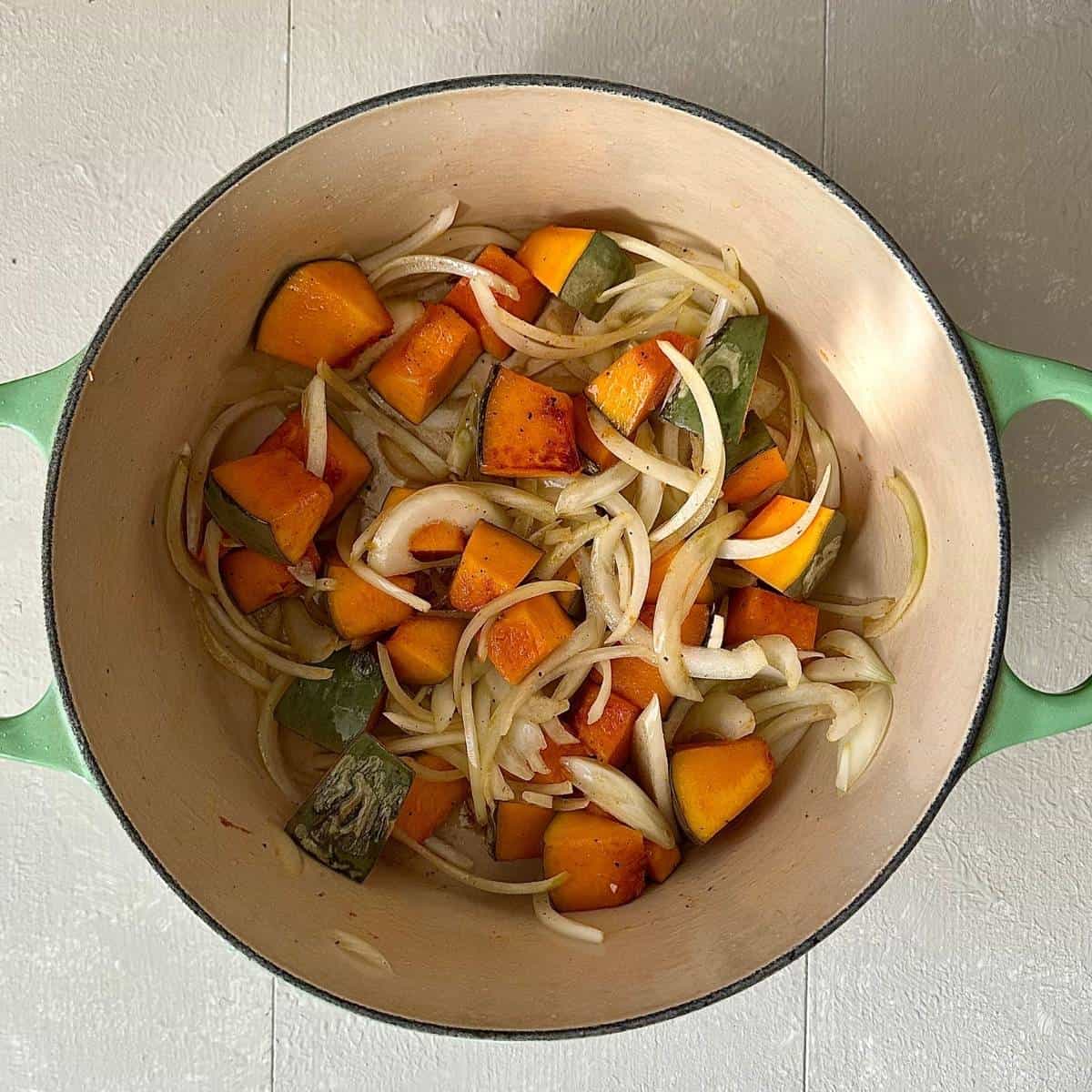 A large green pot containing chunks of crown prince pumpkin and thinly sliced onion after cooking, for veggie kimchi jjigae