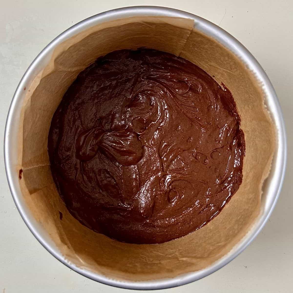 Dark chocolate mud cake mix in a metal cake tin lined with parchment paper, ready to bake.