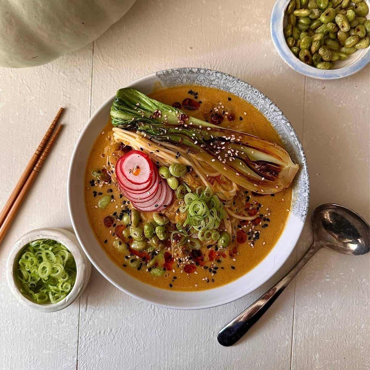 A white bowl containing veggie ramen garnished bok choy, edamame, spring onion and radish.