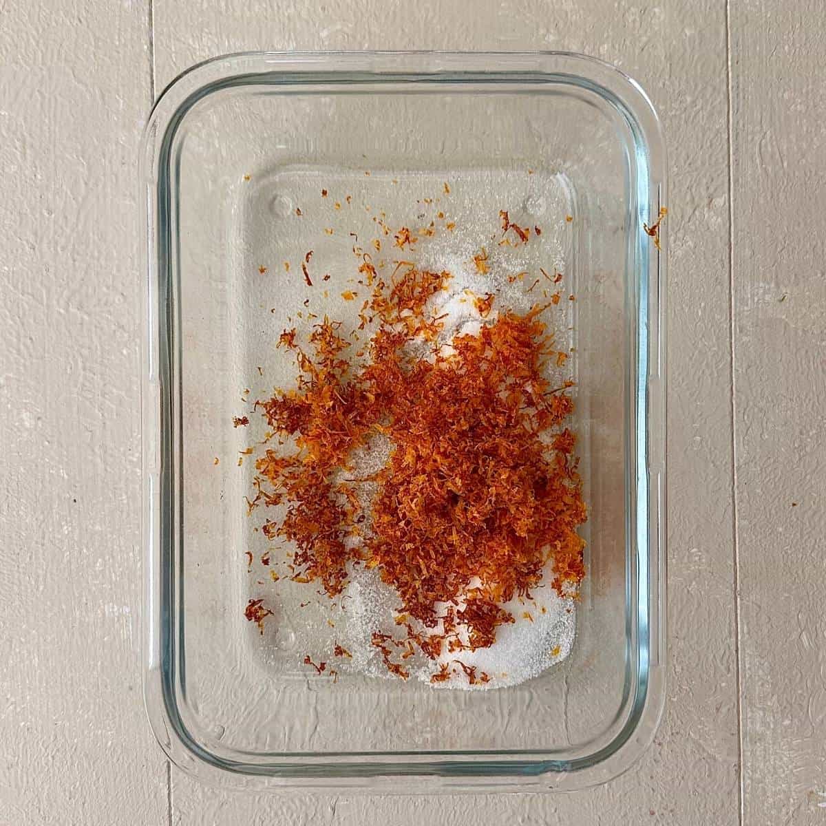 A rectangular glass dish with containing sugar and blood orange zest for blood orange granita.