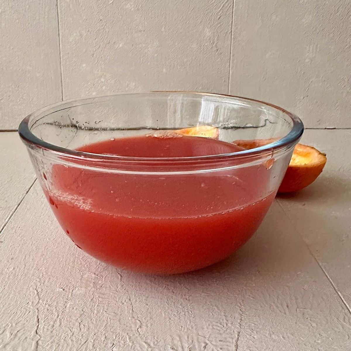 A round glass bowl containing the juice of blood oranges for blood orange granita recipe.