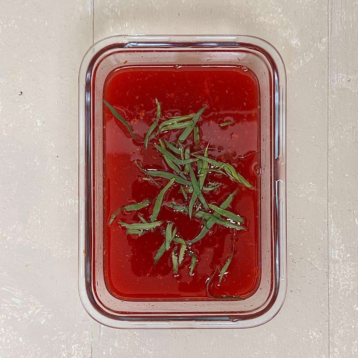 A shallow glass dish containing blood orange granita granita mix - sugar dissolved in bold orange just with blood orange zest and tarragon leaves, ready to freeze.