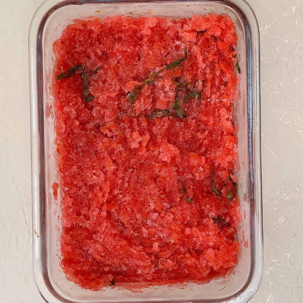 A glass dish containing blood orange granita with tarragon, after freezing and scraping cycles with a fork to create the classic granita texture.