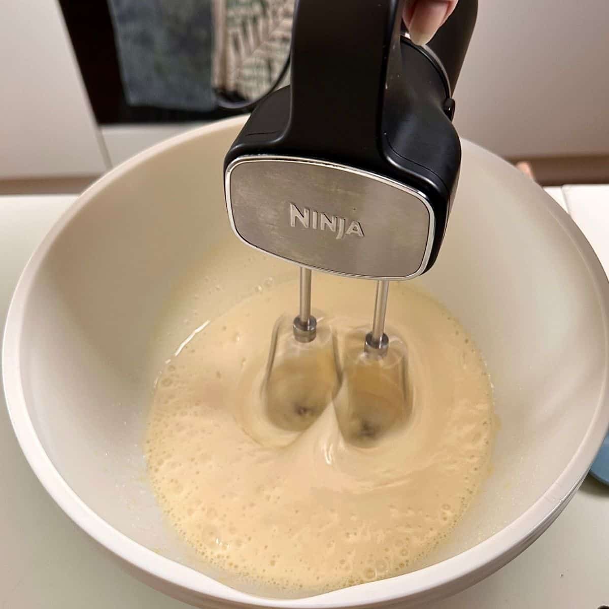 A bowl containing egg and sugar being beaten with an electric whisk for a dark chocolate mud cake recipe.