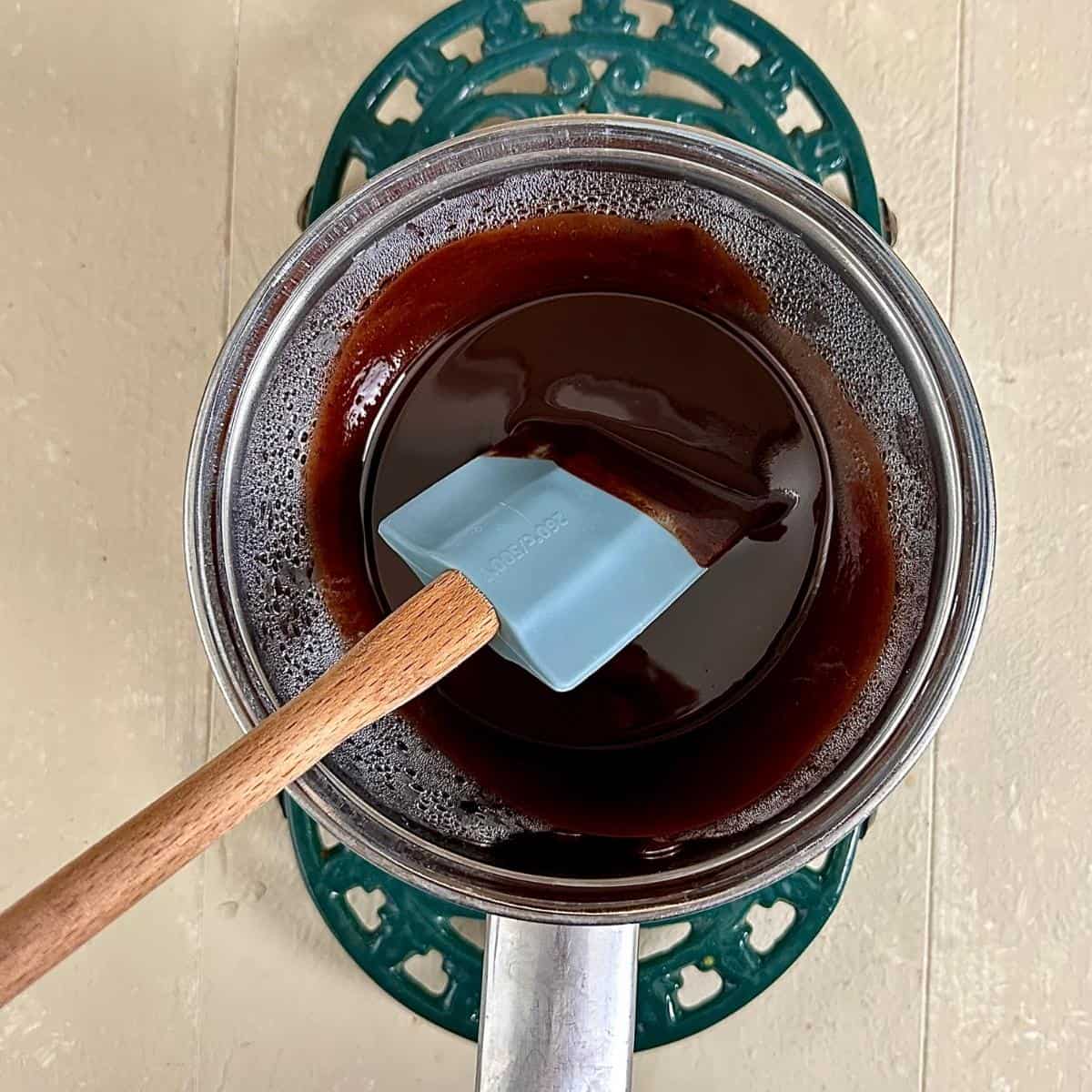 A metal saucepan with a glass bowl inside over hot water. Melted chocolate and butter is in the glass bowl. A spatula sits in the melted chocolate and butter.