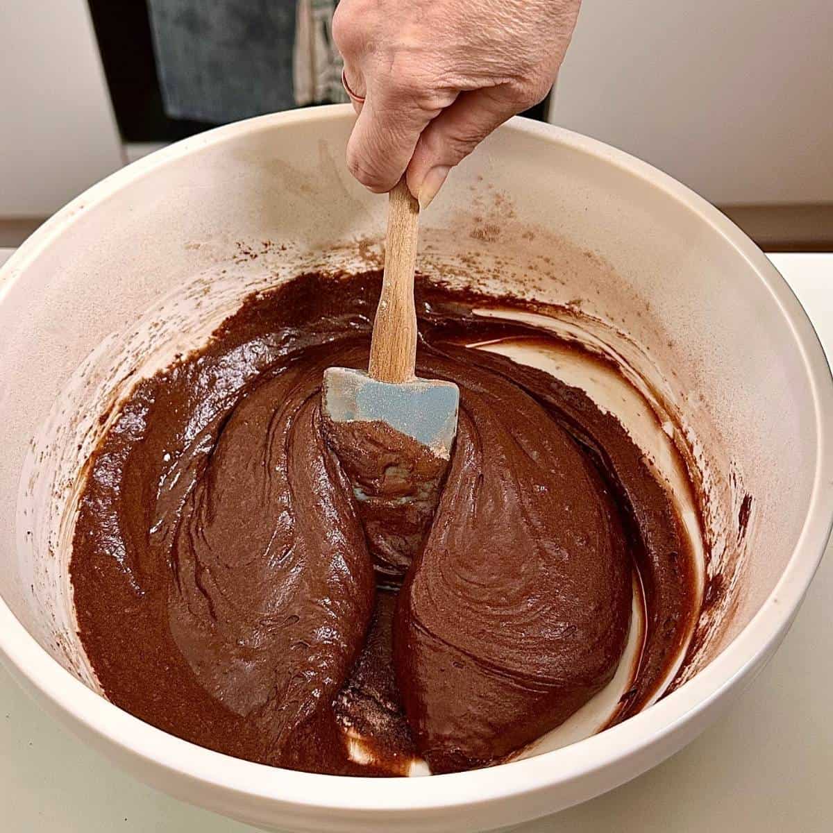 A bowl containing cake mix for a dark chocolate mud cake. A spatula it being used to fold the cake mix.