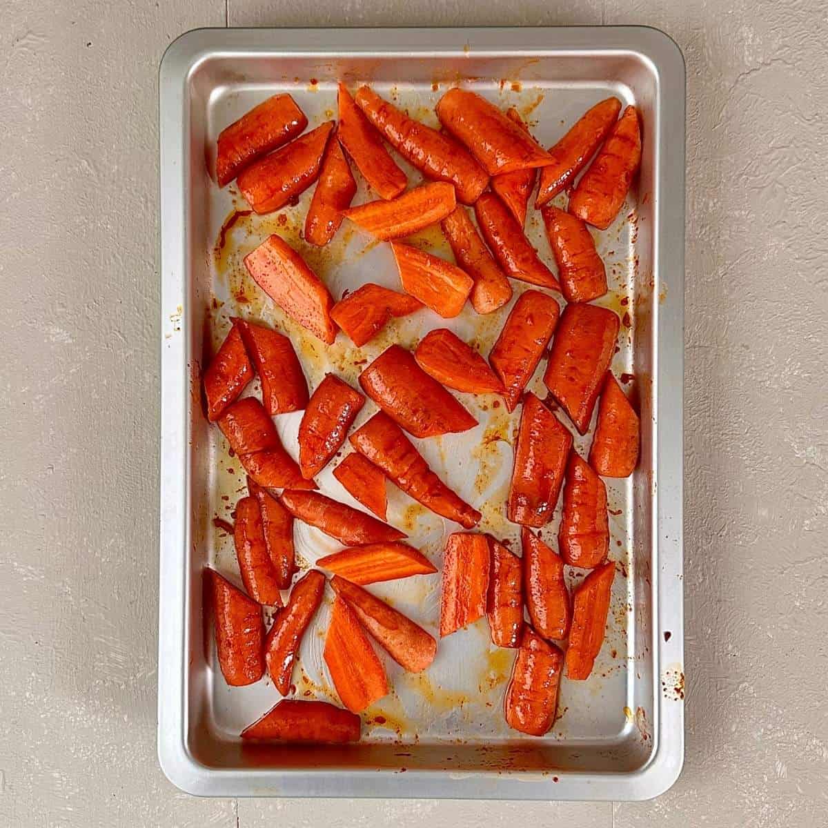 A metal baking tray containing chopped carrots coating in olive oil and gochujang paste ready for roasting for gochujang roasted carrots recipe.